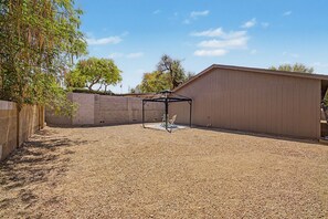 Ein Garten mit Kiesbefestigung, einem Metallpavillon und einem Holzschuppen.