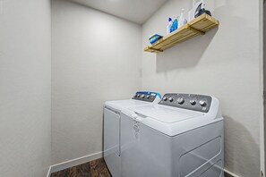 Ein Waschraum mit einer Waschmaschine mit Frontlader und einem darüberliegenden Regal für Reinigungsmittel.