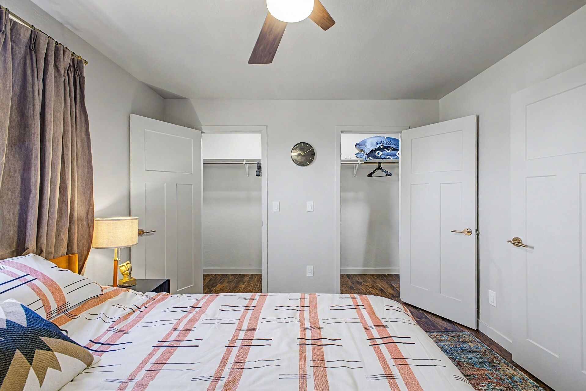 A bedroom with a bed, a ceiling fan, a clock, and a wardrobe.