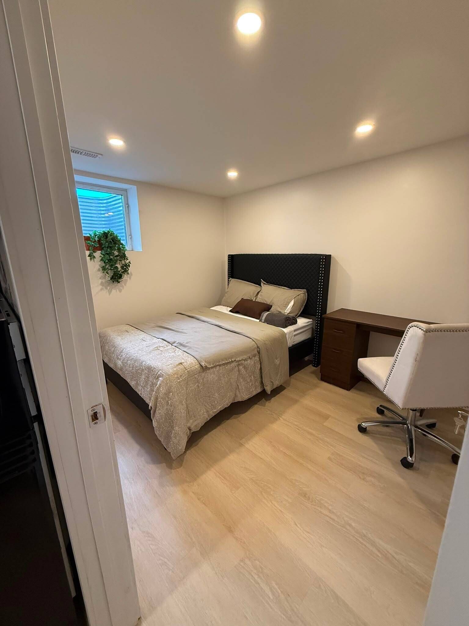 A bedroom with a bed, bedside table, chair, and a window with blinds.