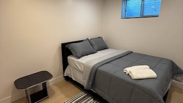 A bedroom with a bed, a bedside table, a window, and a small bench.