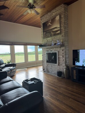 A living room with a stone fireplace, a television, and a leather sofa. - Peaceful Four-Bedroom Country Retreat with Hot Tub & InfraredSauna (Parkville)
