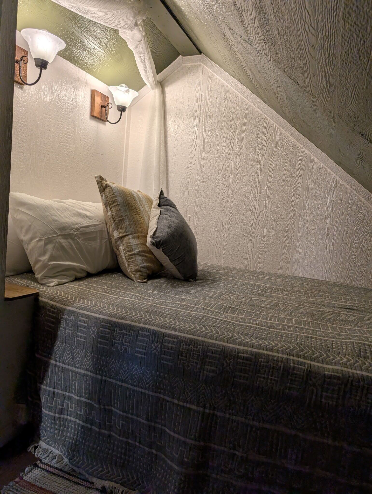 A cozy attic bedroom with a sloped ceiling, a patterned bedspread, and two pillows.