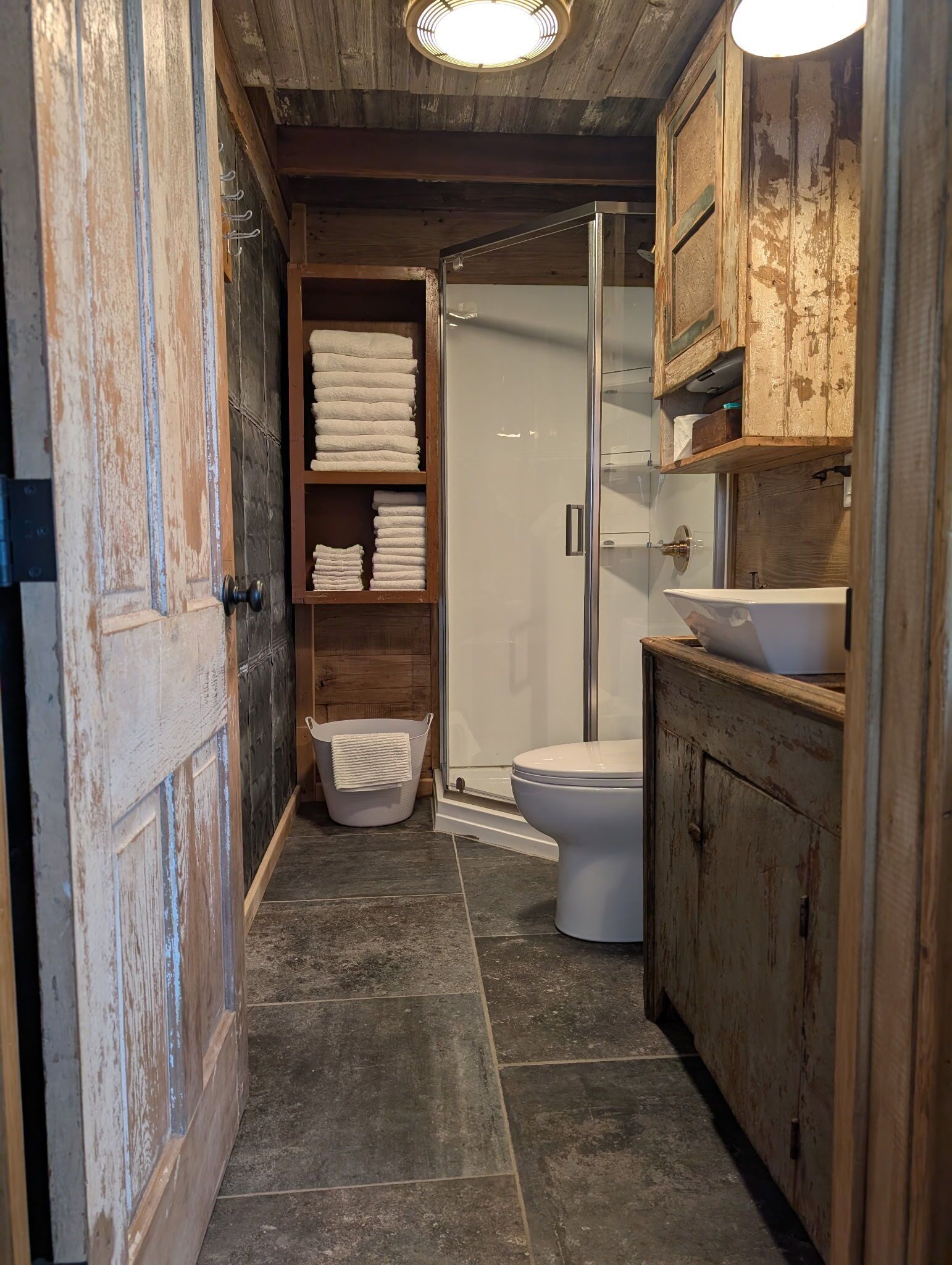 Un baño estrecho con ducha, inodoro y armarios de madera.