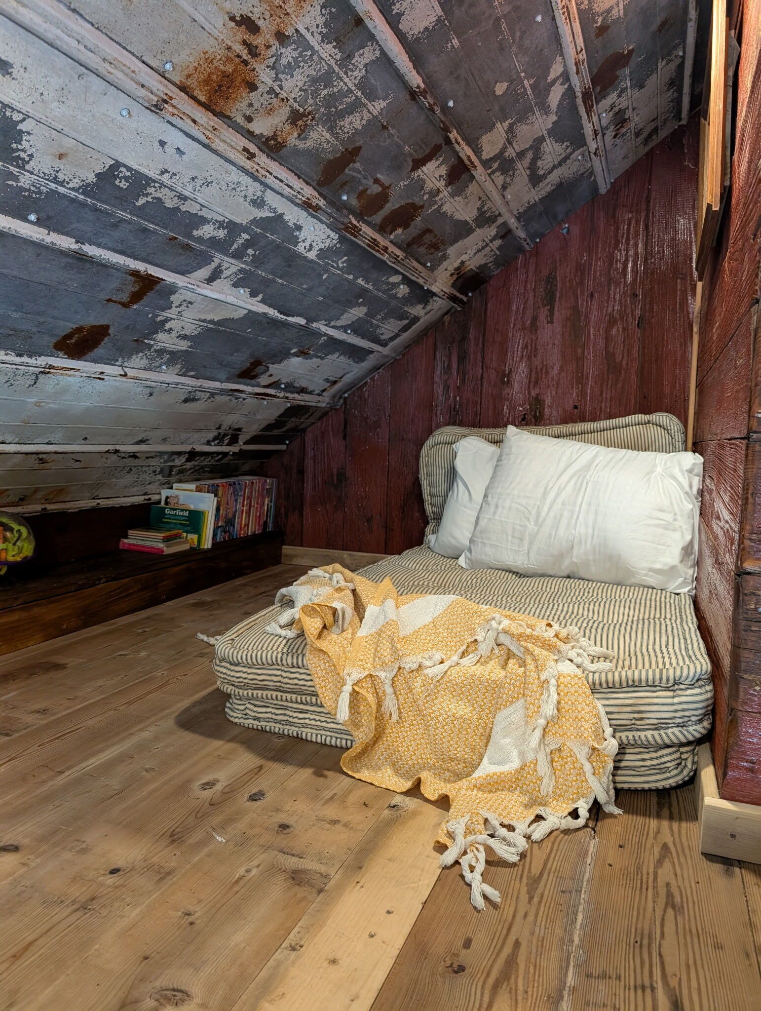 A cozy attic bedroom with a bed, pillows, a blanket, and a bookshelf with books.