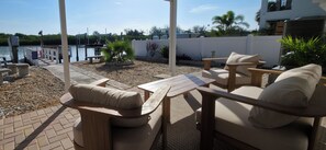An outdoor patio with a table and chairs, a view of a body of water, and a white fence. - Private Waterfront House • Private Dock • 2 Min Walk to Beach (Indian Shores)