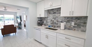 A modern kitchen with white cabinets, a stone backsplash, and a built-in dishwasher. - Private Waterfront House • Private Dock • 2 Min Walk to Beach (Indian Shores)