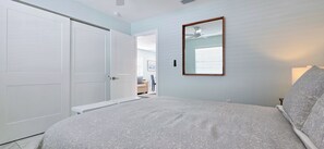 Een slaapkamer met een bed, een deur, een spiegel en een plafondventilator.