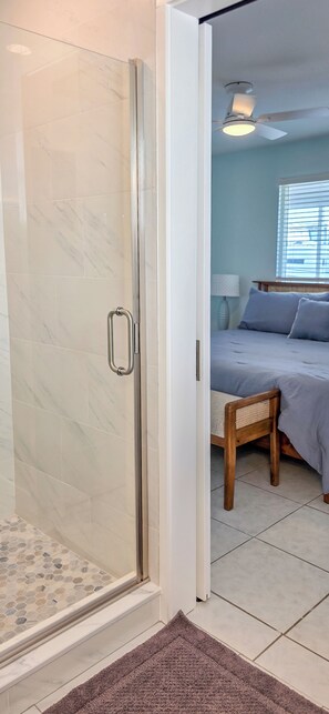 A room with a glass shower door, a bed with a wooden headboard, and a window with blinds. - Private Waterfront House • Private Dock • 2 Min Walk to Beach (Indian Shores)
