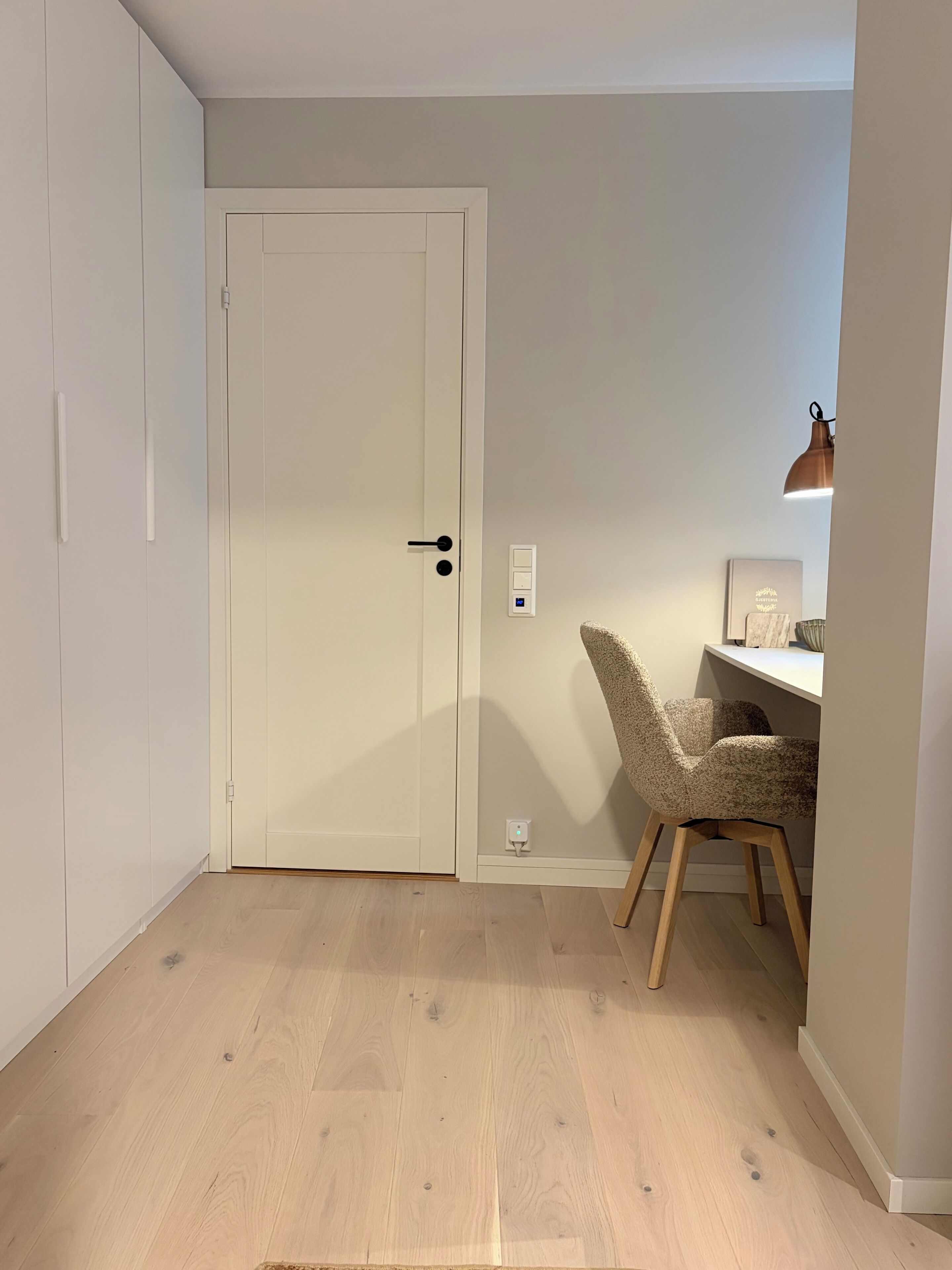 A room with a closed door, a desk with a chair, and a lamp.