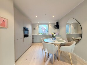 Une cuisine moderne avec un coin repas, comprenant une table ronde entourée de chaises, un vase avec des fleurs et un grand miroir au mur.
