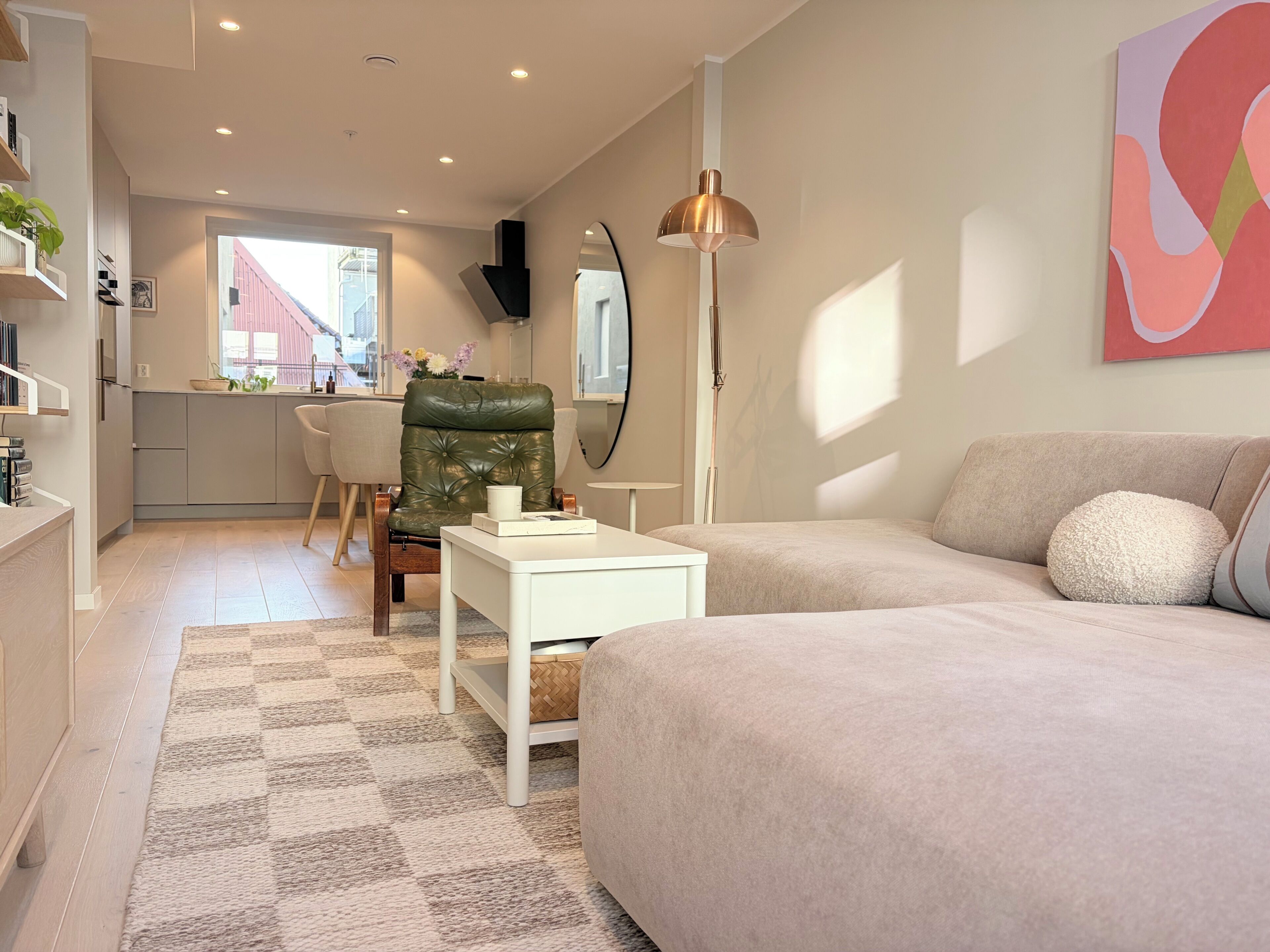 Un salon moderne avec un canapé, une table basse et un fauteuil. On aperçoit, au fond, un coin cuisine avec une fenêtre.