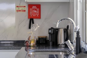 Uma cozinha com pia, cafeteira e extintor de incêndio na parede.