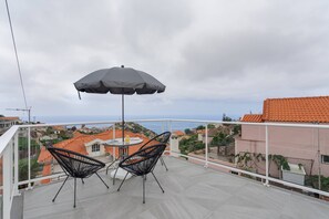 Een balkon met twee zwarte stoelen, een tafel en een grijze parasol.