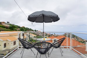 Un balcon avec une table et deux chaises, un parasol et une vue sur une ville côtière.