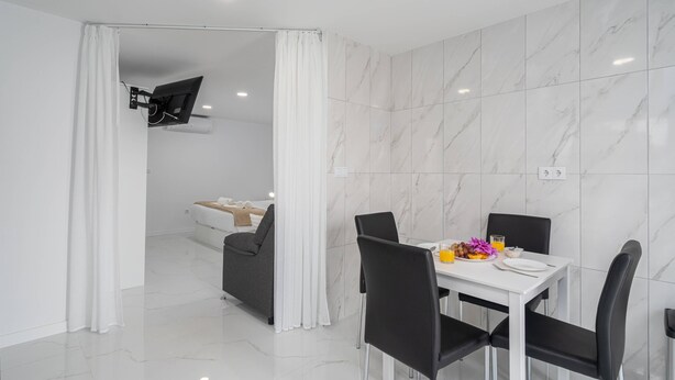 Un comedor moderno con una mesa blanca, sillas negras y una cortina blanca.