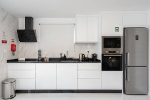 A modern kitchen with white cabinets, a stainless steel refrigerator, and a built-in oven. - Branco's Apartment 03 by GALMI (Ponta do Sol)