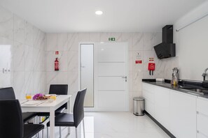 Une cuisine moderne avec des armoires blanches, un comptoir noir et un évier en acier inoxydable. On y trouve une table à manger avec des chaises, et un extincteur fixé au mur.
