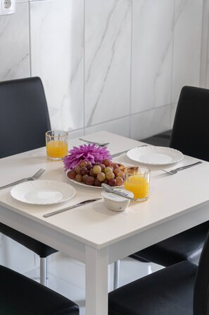 A dining table with plates, cutlery, a bowl of fruit, and glasses of orange juice. - Branco's Apartment 03 by GALMI (Ponta do Sol)