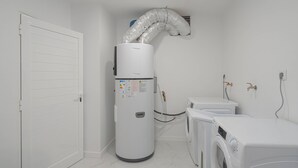 Un cuarto de lavado con una secadora industrial grande, una lavadora y un calentador de agua con una manguera flexible.