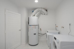 A laundry room with a large industrial dryer, a washing machine, and a water heater with a flexible hose. - Branco's Apartment 03 by GALMI (Ponta do Sol)