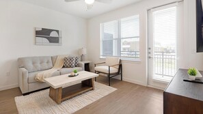 A modern living room with a sofa, a coffee table, a chair, and a TV. - Landing | Stylish 1BD, Pool, Courtyard (Dallas)