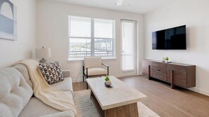 Ein modernes Wohnzimmer mit einer Couch, einem Sessel, einem Couchtisch und einem an der Wand befestigten Fernseher.
