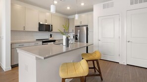 A modern kitchen with a central island, stainless steel appliances, and two bar stools. - Landing | Stylish 1BD, Pool, Courtyard (Dallas)
