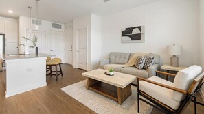A modern living room with a sofa, coffee table, and chairs. There is a kitchen area with a sink and a dining table. - Landing | Stylish 1BD, Pool, Courtyard (Dallas)