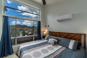A bedroom with a large window, a bed with patterned bedding, a nightstand with a lamp, and an air conditioning unit on the wall. - Stargazing Dome Climbing Wall Zion & Bryce (Glendale)