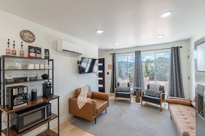 A modern living room with a sofa, a coffee station, a flat-screen TV, and a large window with curtains. - Stargazing Dome Climbing Wall Zion & Bryce (Glendale)
