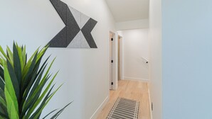 Käytävällä on geometrisesti kuvioitu seinätaideteos, ruukussa oleva kasvi ja ovi, joka johtaa toiseen huoneeseen.