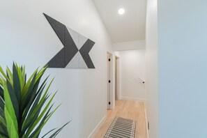 A hallway with a geometric wall art piece, a potted plant, and a door leading to another room. - Stargazing Dome Climbing Wall Zion & Bryce (Glendale)