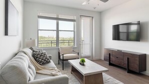 A modern living room with a sofa, a coffee table, a TV, and a cabinet. - Landing | Stylish 2BD, Pool, Gym (Dallas)