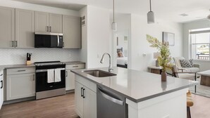 Et moderne køkken med en central ø, stålstål-hvidevarer og udsigt til det tilstødende opholdsstue.
