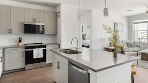 A modern kitchen with a central island, stainless steel appliances, and a view into the adjacent living area. - Landing | Incredible 2BD, Courtyard, Clubhouse (Dallas)