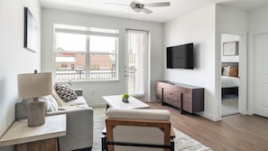 A modern living room with a sofa, a coffee table, a TV, and a dining area. - Landing | Incredible 2BD, Courtyard, Clubhouse (Dallas)
