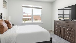 A bedroom with a bed, a dresser, a television, and a window with a view of a building. - Landing | Modern 2BD, Pool, Gym (Dallas)