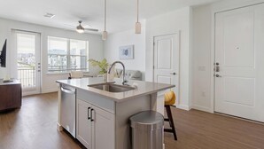 A modern kitchen with a central island, a dishwasher, and a trash can. - Landing | Chic 1BD, Gym, Courtyard (Dallas)