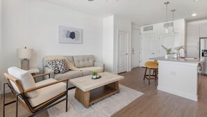 A modern living room with a sofa, coffee table, and chairs, a kitchen with a bar area, and a dining table with chairs. - Landing | Chic 1BD, Gym, Courtyard (Dallas)