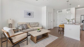 Ein modernes Wohnzimmer mit Sofa, Couchtisch und Sesseln, eine Küche mit Barbereich und ein Esstisch mit Stühlen.
