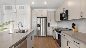 A modern kitchen with stainless steel appliances, white cabinetry, and a herringbone tile backsplash. - Landing | Chic 1BD, Gym, Courtyard (Dallas)