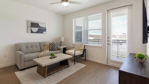 A living room with a sofa, coffee table, chair, and a painting on the wall. - Landing | Amazing 1BD, Courtyard, Clubhouse (Dallas)