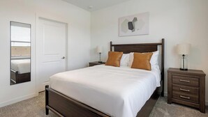 Un dormitorio con cama, mesita de noche, lámpara, espejo y una obra de arte en la pared.