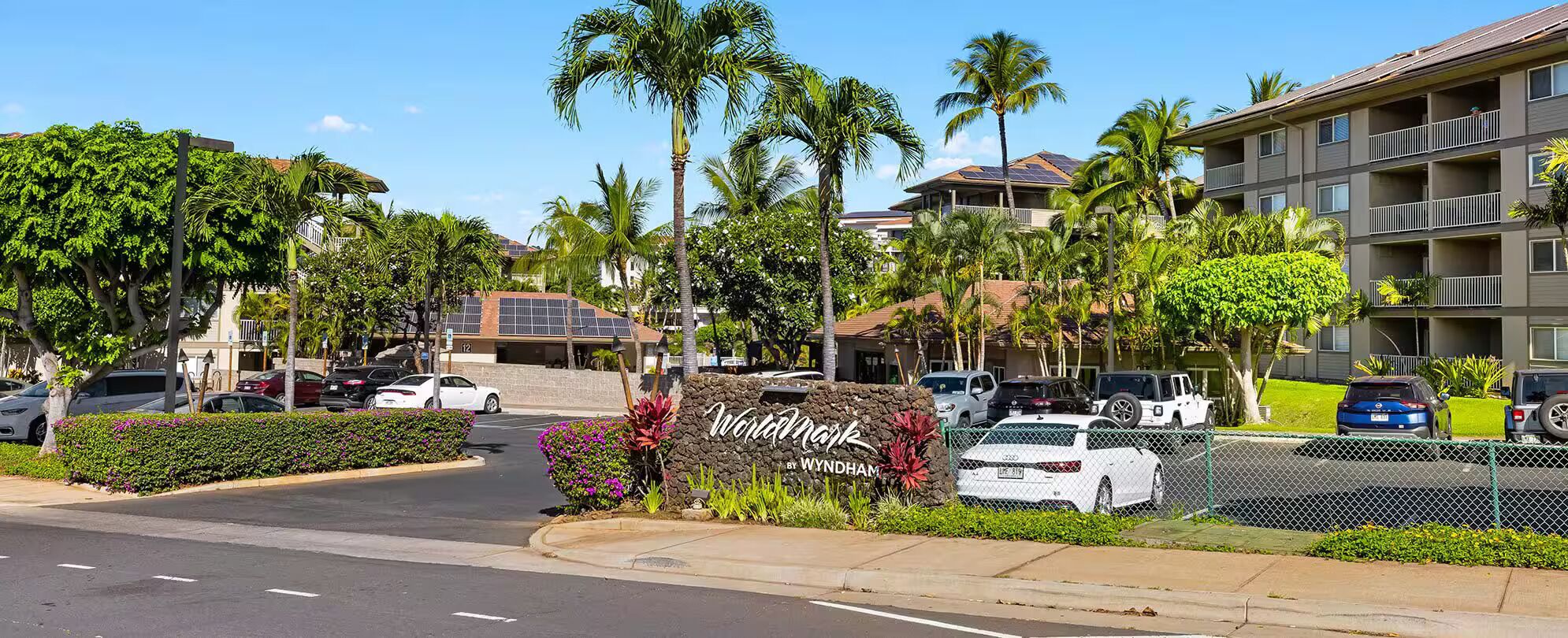 A hotel entrance with a sign, parked cars, and a well-maintained lawn.