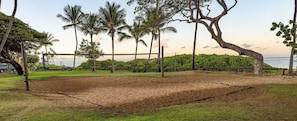 A sandy volleyball court surrounded by palm trees and a fence, with a view of the ocean in the background. - 2-bedroom, 2-bathroom resort at Worldmark Kihei Hawaii (Kihei)