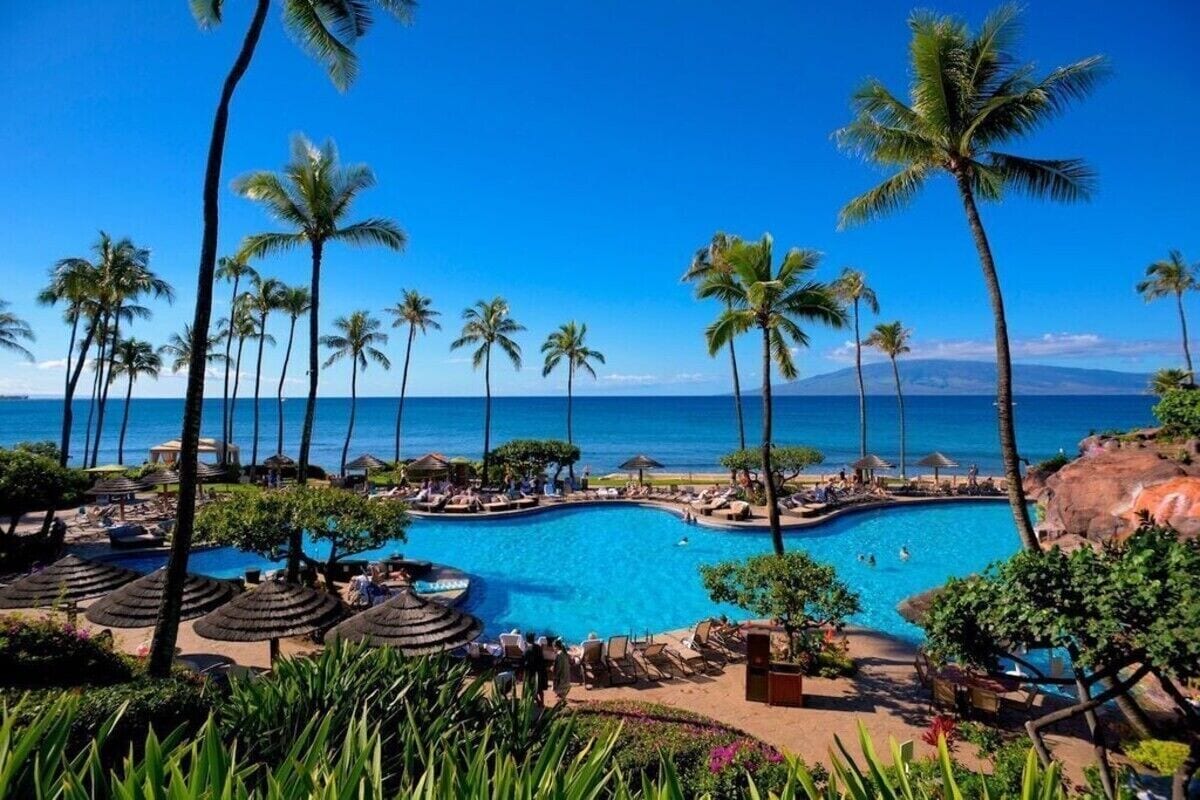 A resort with a large pool surrounded by palm trees and lounge chairs.