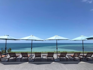 Una terraza con sillones de descanso y sombrillas con vista a un mar azul y despejado.