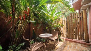 A patio with wicker furniture and a table, surrounded by lush tropical plants and a wooden fence. - Pousada Montão Do Trigo (São Sebastião)