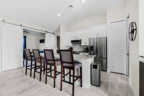 Une cuisine moderne avec des meubles blancs, un réfrigérateur en acier inoxydable et un coin bar doté de chaises en bois.